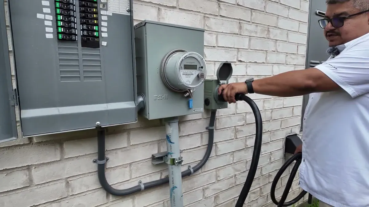 Pro Max Electrical plugging a generator cord into a new inlet box beside the meter on a brick house