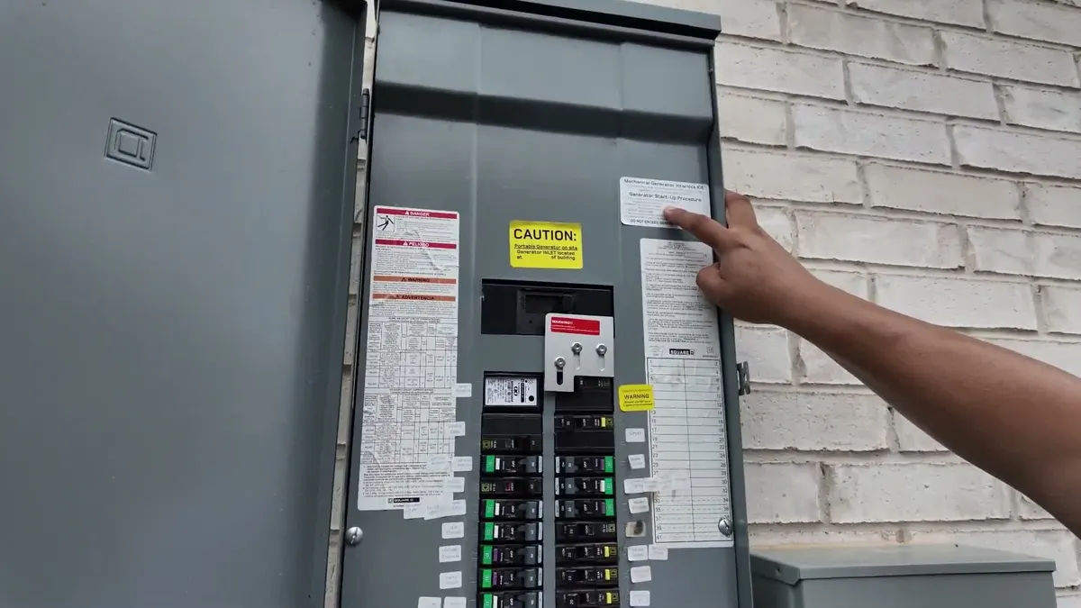 Pointing at the labeled breakers and caution sticker inside the panel door