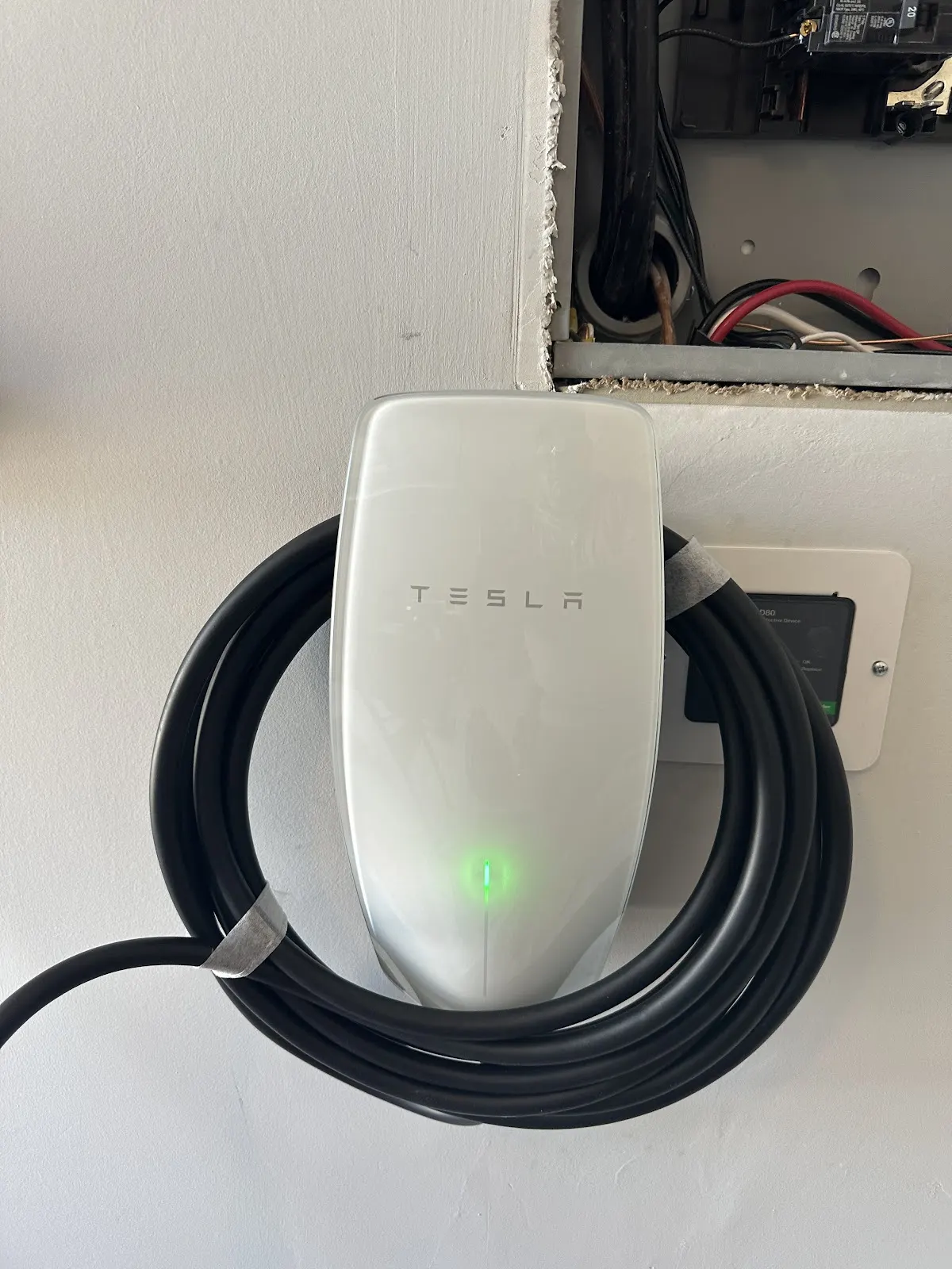 White Tesla Wall Connector mounted in a garage with its cable coiled, installed by Pro Max Electrical